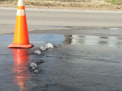 Orange cone marks water flowing from leak under a street